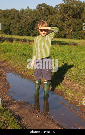 Ein MODEL Release sieben Jahre alter Junge steht in einer Pfütze mit Hunter Wellies auf im Vereinigten Königreich Stockfoto