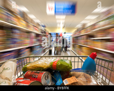 Blick über einen geladenen Einkaufswagen, da es einen Gang hinunter gedrückt wird Stockfoto