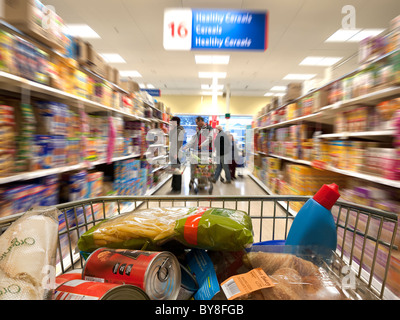 Blick über einen geladenen Einkaufswagen, da es einen Gang hinunter gedrückt wird Stockfoto