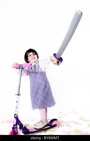 Kleines Mädchen in ihrem Roller und ein Spielzeug Schwert in seiner Hand hetzen Stockfoto