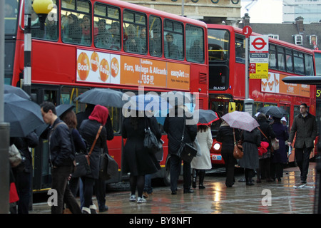 Eine Schlange von Menschen warten im Regen einen Bus im Londoner morgendlichen Berufsverkehr in Waterloo, London an Bord Stockfoto