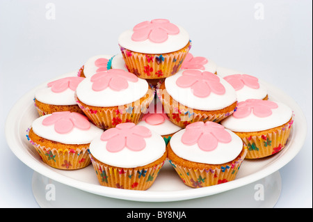 Stapel kleiner Cupcakes, auch bekannt als Brötchen, mit weißer Glasur, verziert mit rosa Fondant-Blumen. Stockfoto