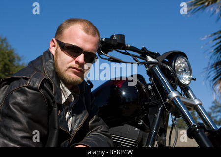 Biker posiert vor seinem Motorrad in schwarzer Lederjacke mit einem ernsten Blick. Stockfoto