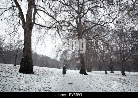 Eine Frau zu Fuß durch den Green Park, London, im Schnee. Ein graues Eichhörnchen läuft über den Weg Stockfoto