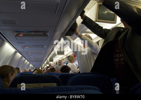 Passagiere vorbereiten für Flug, indem verstauen Handgepäck Gepäck im Gepäckfach in Flugzeug Stockfoto