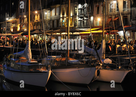 Segelboote und Touristen an Straßencafés / Bürgersteig Cafés entlang des Kais der Honfleur Hafen bei Nacht, Normandie, Frankreich Stockfoto