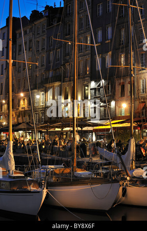 Segelboote und Touristen an Straßencafés / Bürgersteig Cafés entlang des Kais der Honfleur Hafen bei Nacht, Normandie, Frankreich Stockfoto