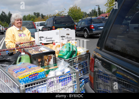 Ältere Frau mit zwei Einkaufswagen voller Haushalt Waren auf dem Parkplatz von costco. Stockfoto