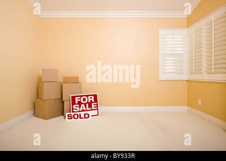Umzugskartons zu verkaufen und verkauft Immobilien-Zeichen am Boden im leeren Raum mit textfreiraum auf leere Wand. Stockfoto