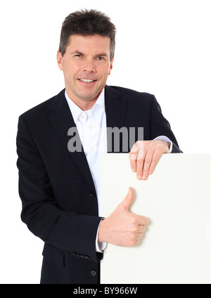 Attraktiver Mann mittleren Alters machen Daumen hoch-Zeichen neben einem weißen Brett. Alle auf weißem Hintergrund. Stockfoto