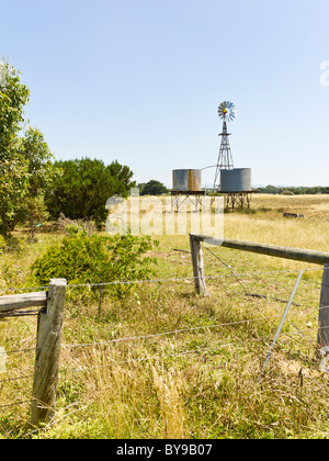 Stacheldrahtzäune und Bohrung Wasser Windmühle im Hintergrund, im australischen ländlich geprägtes Land Stockfoto