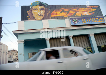 Alte amerikanische Oldtimer vorbei mit einem Poster von Che Guevara auf ein Gebäude in einer Straße von Cienfuegos, Kuba. Stockfoto