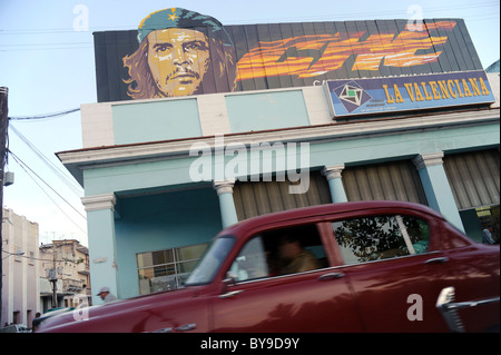 Alte amerikanische Oldtimer vorbei mit einem Poster von Che Guevara auf ein Gebäude in einer Straße von Cienfuegos, Kuba. Stockfoto