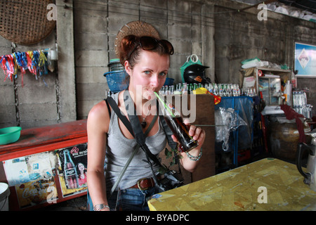 Junge weibliche Touristen trinken Coca Cola mit einem Strohhalm aus einer Flasche, Thailand. Stockfoto