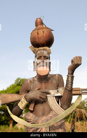 Frau des Stammes Mursi mit einem Gewehr und einem Teller in ihrer Lippe, Mago Nationalpark, Süd Omo-Tal, Südäthiopien Stockfoto