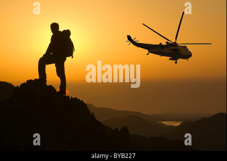 Ein Walker auf Swirl Howe Seenplatte bei Sonnenuntergang UK mit einem Sea King Hubschrauber. Stockfoto