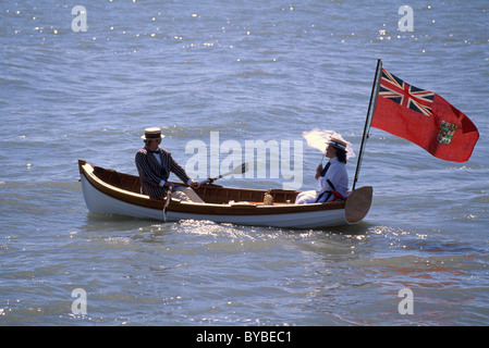 Herr und Dame im historischen Periode Kostüm Rudern im Ruderboot mit historischen Red Ensign Flag Flying - Nachmittag Bootsfahrt Stockfoto