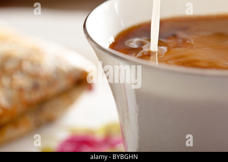 Milch hinzugefügt, um eine Tasse Kaffee, eine isländische Pfannkuchen zweimal mit geschlagener Sahne und Blaubeeren Marmelade neben der Tasse gefaltet. Stockfoto