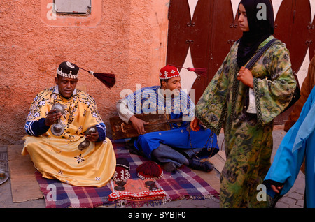 Glücklich Gnawa Straßenmusiker in Marrakesch schwingen ihre Tarbusch Quasten in der Zeit mit der Musik und Frauen Passanten Marokko Stockfoto