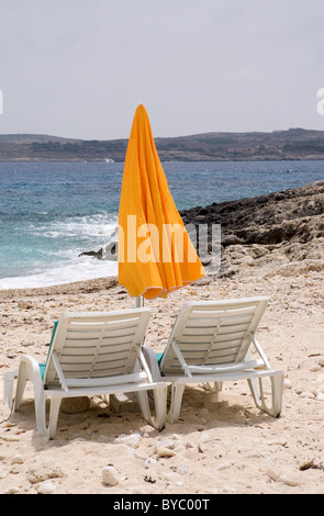 Sonnenliege und Orange Sonnenschirm an einem Sandstrand mit einem blauen Meer und Himmel Hondoq Ir-Rummien Gozo Malta Stockfoto