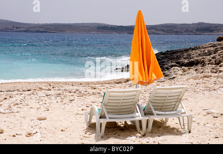 Sonnenliegen und eine orange Sonnenschirm an einem Sandstrand mit blauem Meer und Himmel bei Hondoq Ir-Rummien Gozo Malta Stockfoto