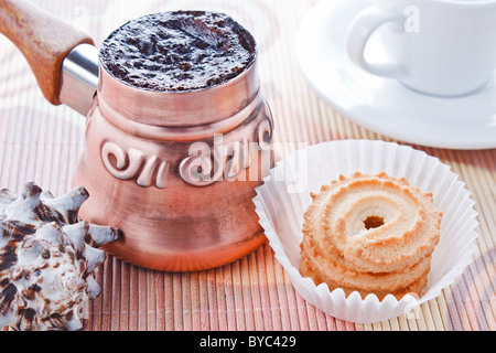 Frisch gebrühter Kaffee Türkisch in Kupfer Kaffeekanne mit Tasse, Keksen und Muschel als Dekoration Stockfoto