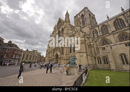 Touristen stehen & Menschen zu Fuß durch York Minster Südeingang (Fotos von Constantine Statue, dramatischen Himmel) - North Yorkshire, England, Großbritannien. Stockfoto