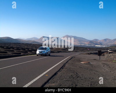 Ein Auto auf der kurvenreichen Straße durch La Geria Weinbauregion von Lanzarote mit dem Dorf Uga in der Ferne Stockfoto