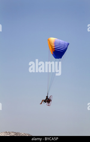 Barfuß Mann Wanderprediger Motor angetrieben Gleitschirm fliegen über einen Hügel vor einem blauen Himmel. Stockfoto