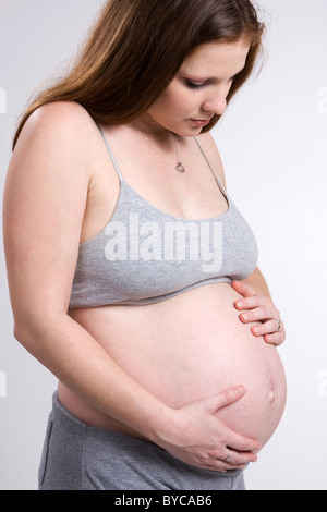 Eine junge schwangere Frau grübelt über ihre Schwangerschaft und ihr Baby bald anzukommen. Stockfoto