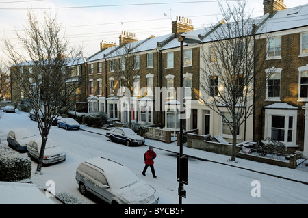 Mann, der entlang der Straße von Mitte Victoria drei-stöckige Reihenhäuser Häuser unter Schnee Holloway N7 Islington London England Großbritannien Stockfoto