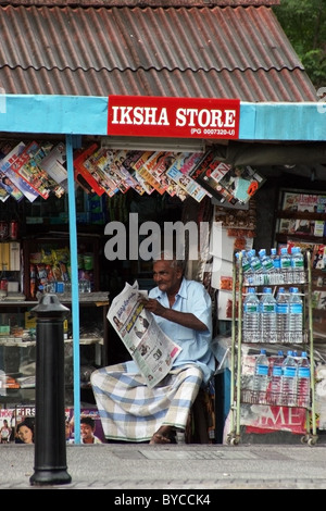 Ein gebildeter asiatischer Mann liest eine malaysische Zeitung in einem kleinen bunten Diverses Geschäft in Georgetown, Penang, Malaysia. Stockfoto