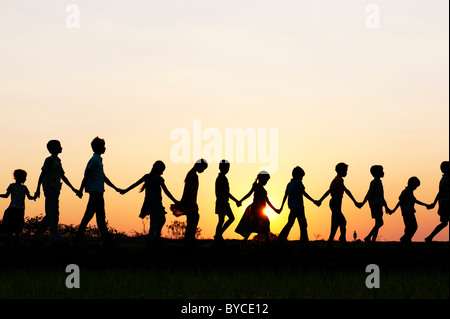 Silhouette indische Mädchen und jungen, die Hand in Hand zu Fuß nach Hause in einem Reisfeld Paddy bei Sonnenuntergang. Andhra Pradesh, Indien Stockfoto