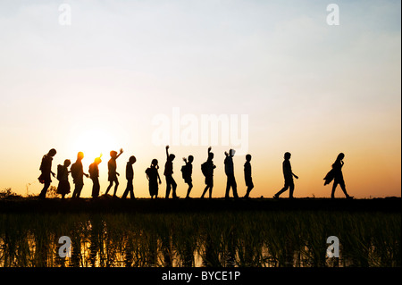 Silhouette indische Mädchen und jungen winken Heimweg von der Schule in einem Reisfeld Paddy bei Sonnenuntergang. Andhra Pradesh, Indien Stockfoto