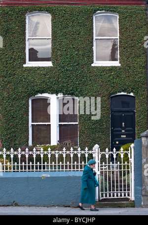 Alle grün, Nationalfarbe Irlands. Eine alte Dame im grünen Mantel Spaziergänge fiel eine Efeu bedeckt Haus in Limerick. Stockfoto