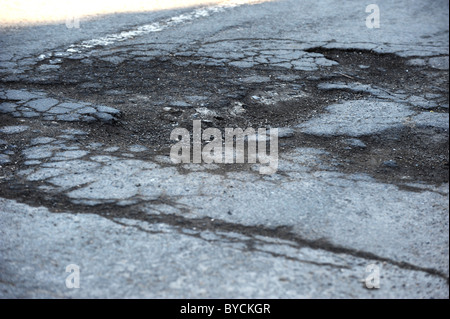 Tiefe Schlaglöcher in einer viel befahrenen Straße, verursacht durch den letzten Schnee und Frost Stockfoto