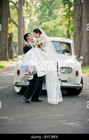 Frisch verheiratet Bräutigam seine neue Braut in seinen Armen hält, wie sie bei ihrer Hochzeitsfeier ankommen. Stockfoto