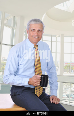 Applying Kaufmann an der Ecke seines Schreibtisches hält eine Kaffeetasse. Stockfoto