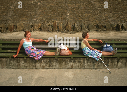 Schwestern sitzen in identische Posen am Deich Bänke auf Blackpool Promenade. Stockfoto