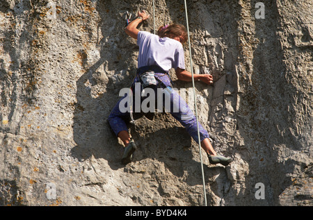 Ein Frau Kletterer auf ein kleines Stück Fels hängt und von Seilen aufgehängt ist. Stockfoto