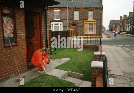 Eine house-proud Hausfrau schneidet ihren Rasen mit einer Schere in Neubauwohnungen auf einem terrassierten Liverpool Street. Stockfoto