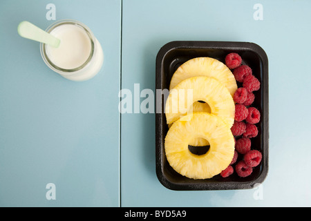 Verpackte Ananasscheiben und Himbeeren mit einer Wanne mit Joghurt Stockfoto