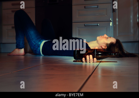 Junge Frau mit einer Bierflasche auf dem Boden der Küche liegend Stockfoto