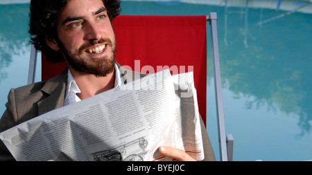 Ein glücklich junger Mann immer am Lächeln und Lachen lesen Papier Swimming Pool Stockfoto