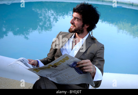 Ein glücklich junger Mann immer am Lächeln und Lachen lesen Papier Swimming Pool Stockfoto