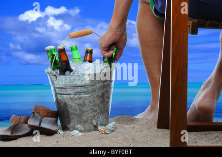 Nahaufnahme eines Mannes sitzen auf einem hölzernen Stuhl am Strand in einen Eimer mit Eis und Bierflaschen zu erreichen. Stockfoto