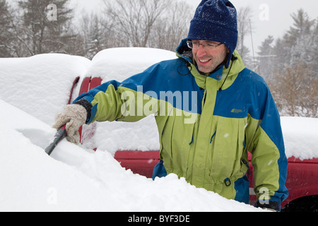 Mann Schaben Schnee vom Auto Windschutzscheibe im Winter Schneesturm, New Hampshire, New England, USA Stockfoto