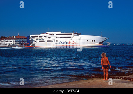 High Speed Ferry Condor Express verlassen Poole Harbour, Poole, Dorset, Mann im Badeanzug auf dem Weg nach Frankreich, beobachtet von gegerbt Stockfoto