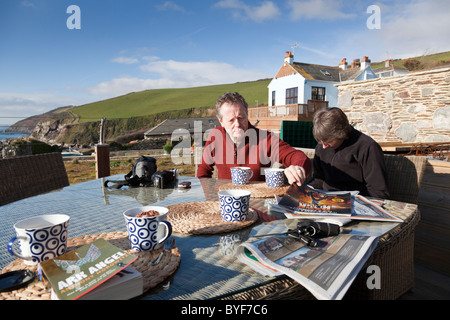 Mann und Frau gelesen das Papier draußen auf einer Terrasse am Meer an einem sonnigen Wintertag in Cornwall, England. Stockfoto