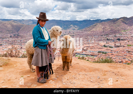 Eine peruanische Frau in traditioneller Kleidung mit ihren Lamas mit Blick auf die Stadt Cusco, Peru, Südamerika. Stockfoto